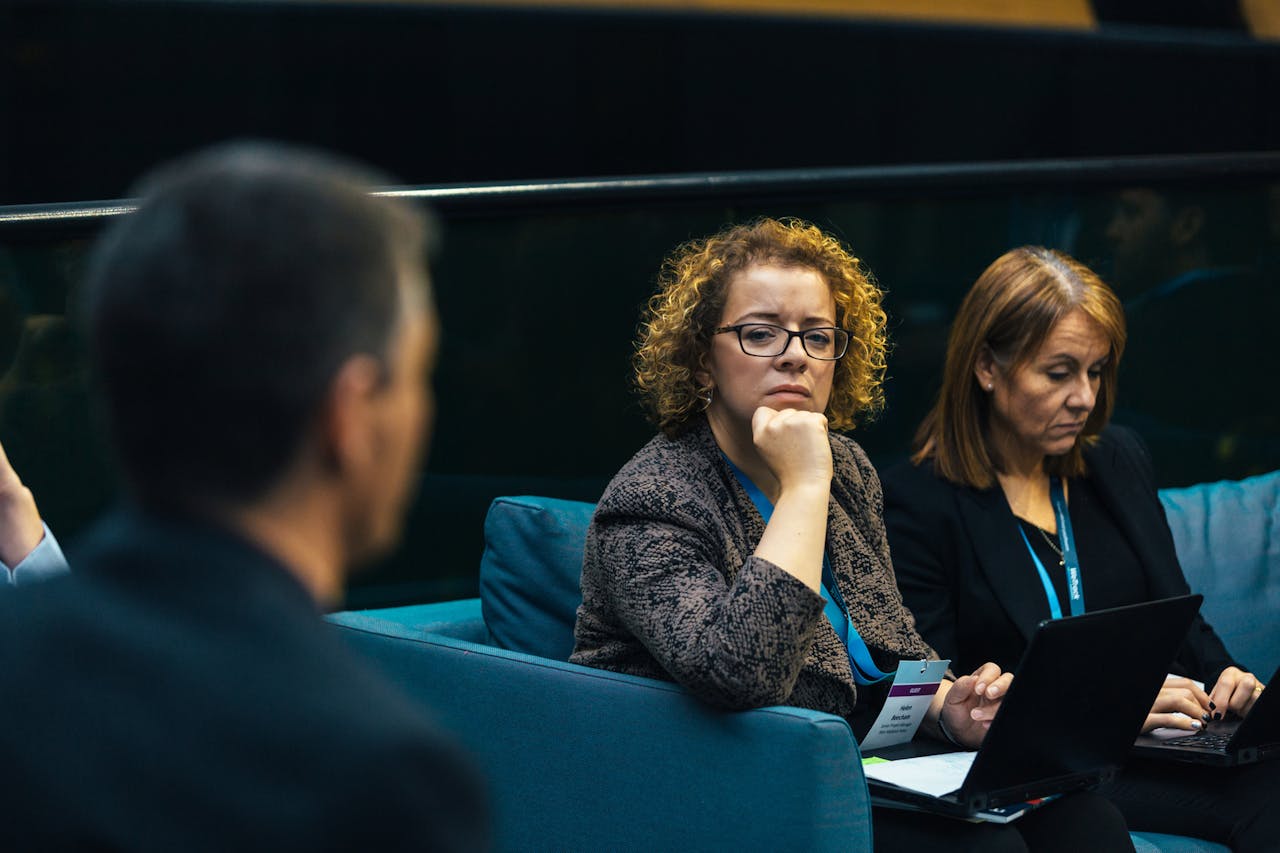 Professionals attending a meeting, listening to a speaker while using laptops 