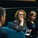 Professionals attending a meeting, listening to a speaker while using laptops