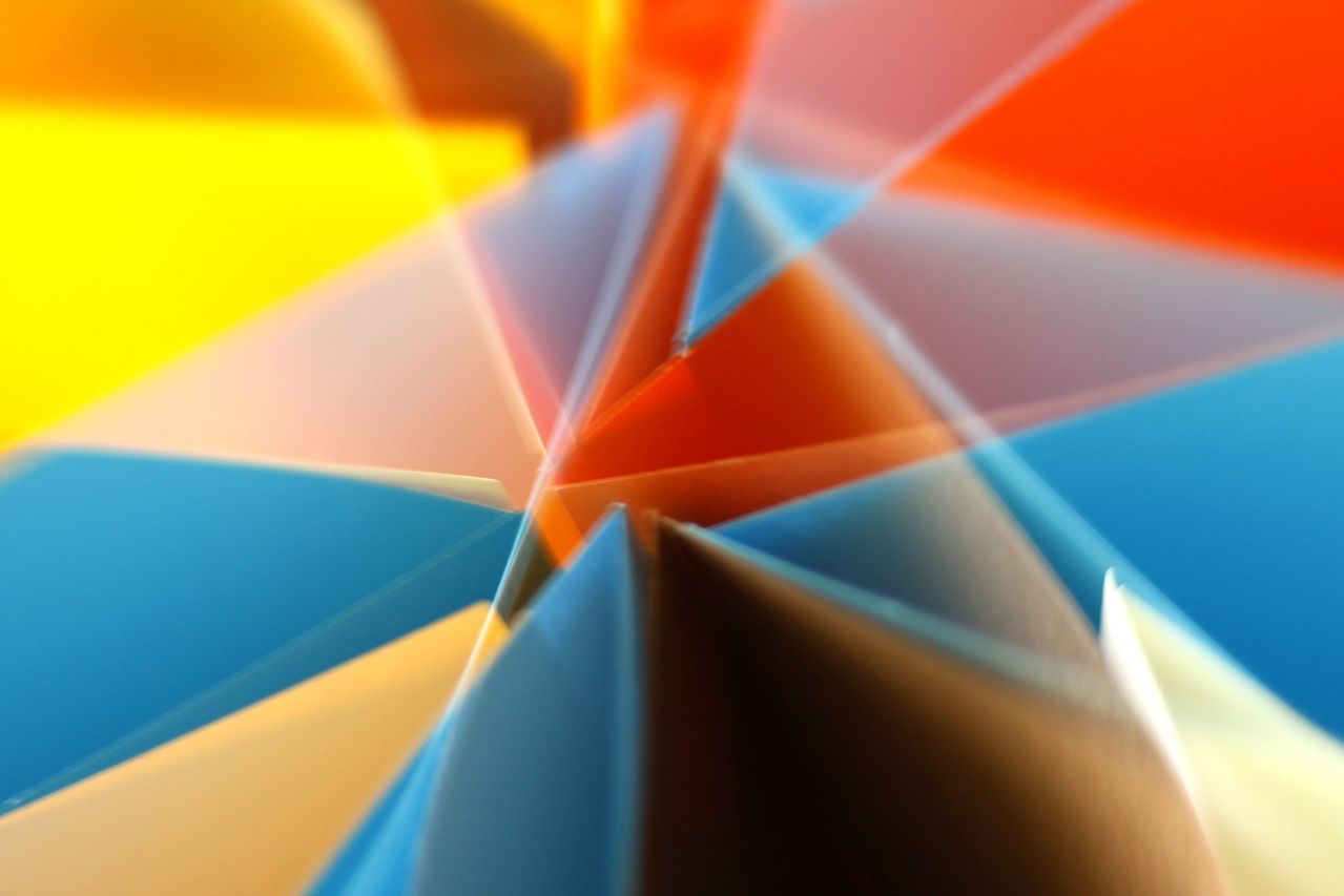 Abstract artwork with overlapping tri-polygonal shapes in orange, yellow, blue, and red, in a layered composition 