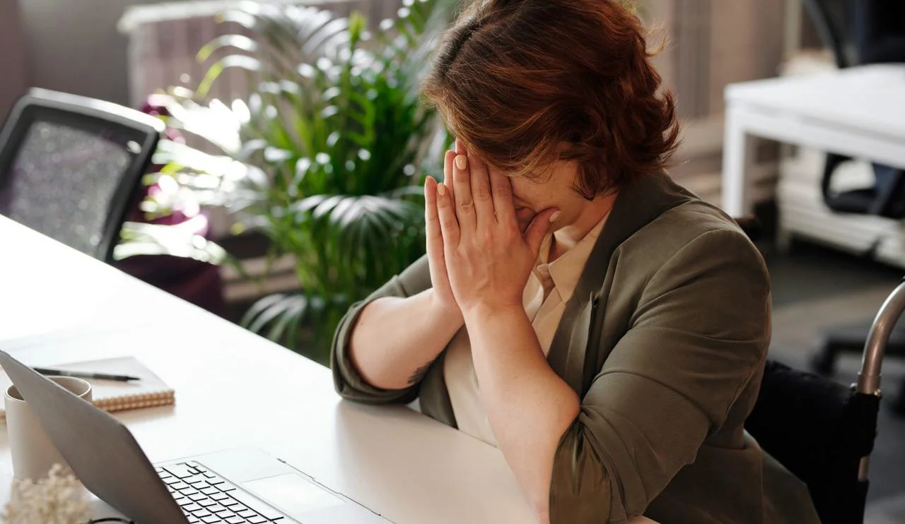 Businesswoman in wheelchair, tired at laptop, symbolizes office stress.
