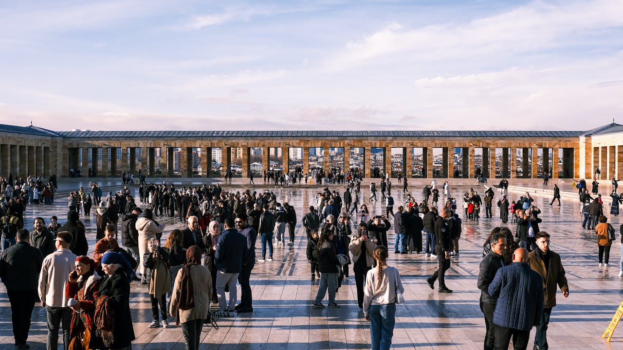 Visitors gather in a large public square framed by a historic colonnade and city views