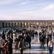 Visitors gather in a large public square framed by a historic colonnade and city views