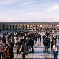 Visitors gather in a large public square framed by a historic colonnade and city views