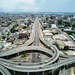 Aerial view of a multi-level highway interchange with cars and surrounding buildings in a dense urban area.