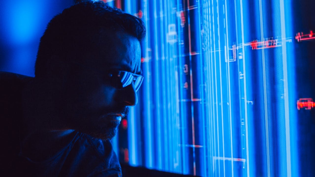 Close-up side profile of a person wearing glasses, looking at a blue digital interface with data lines and charts