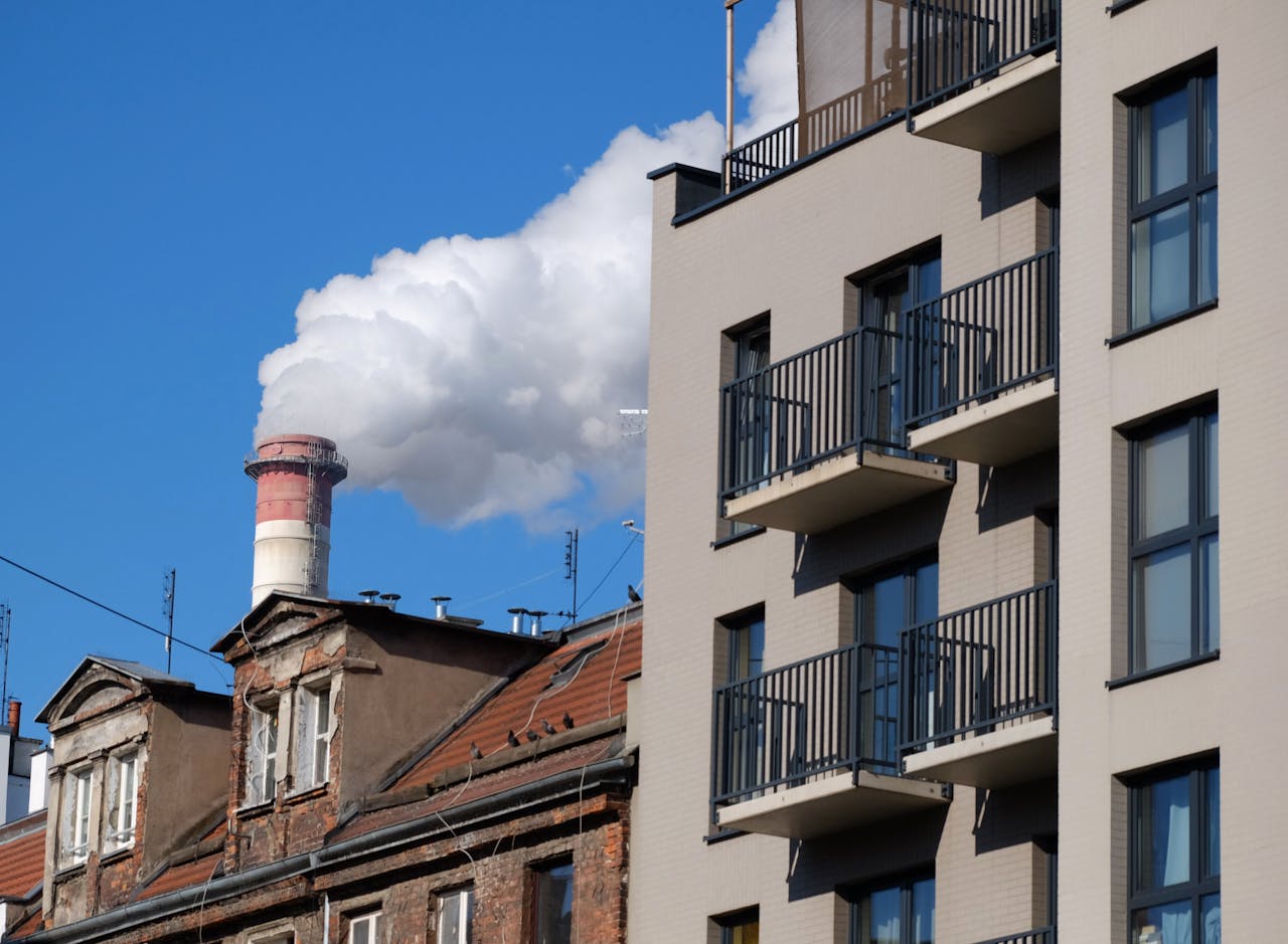 Modern building next to older housing and an industrial chimney releasing smoke