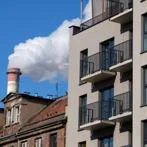 Modern building next to older housing and an industrial chimney releasing smoke