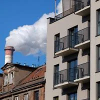 Modern building next to older housing and an industrial chimney releasing smoke
