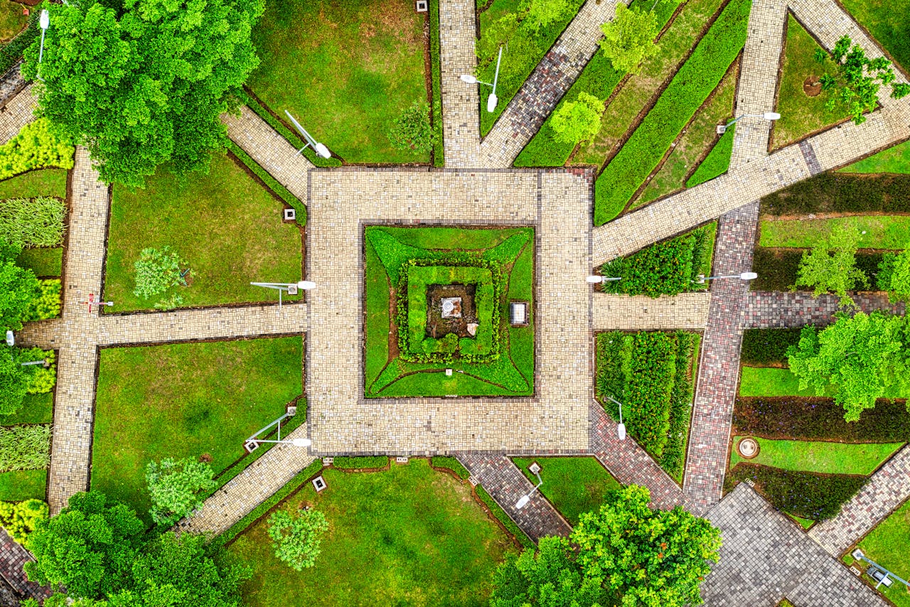 Top-down view of a landscaped park featuring intersecting paved walkways, green lawns, trees,