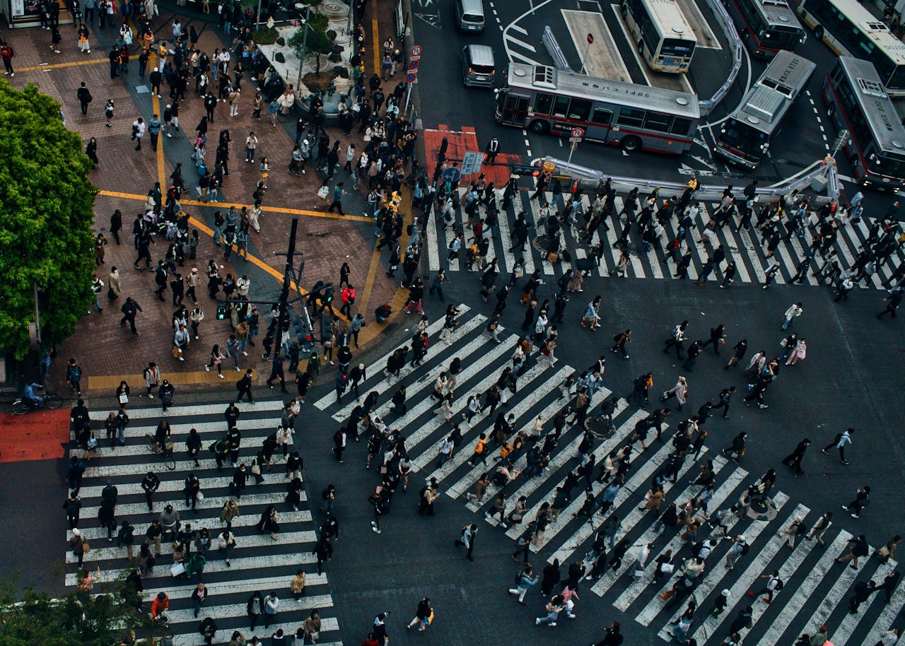 Top-down view of a crowded urban crosswalk with many people walking across multiple zebra crossings