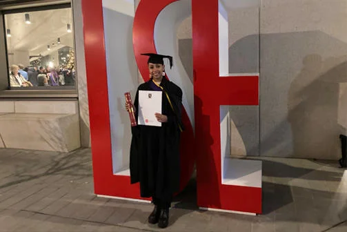 Phaedra Haringsma stands with her degree wearing her graduation robes