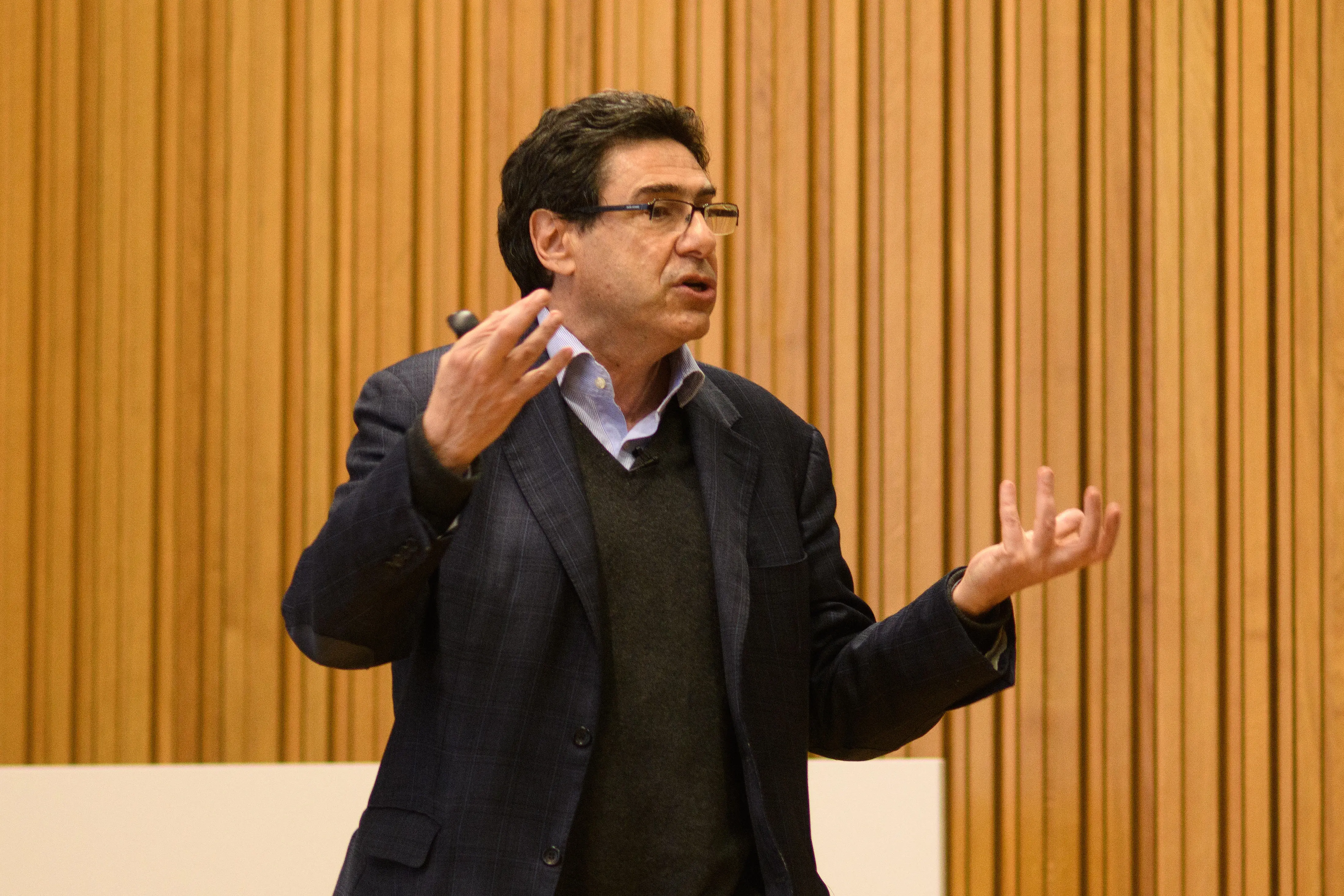 Philippe Aghion stands giving a talk. Behind him is a wood panelled wall.
