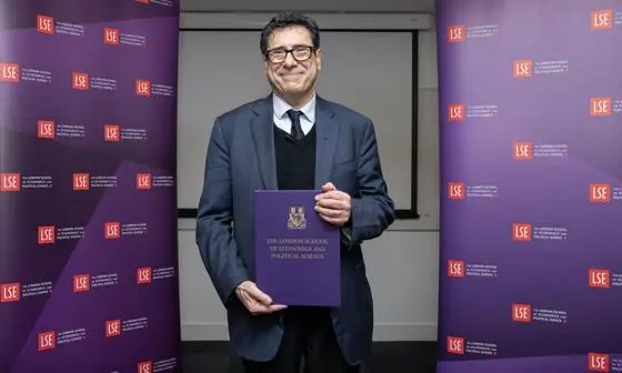 Philippe Aghion, standing between two LSE banners