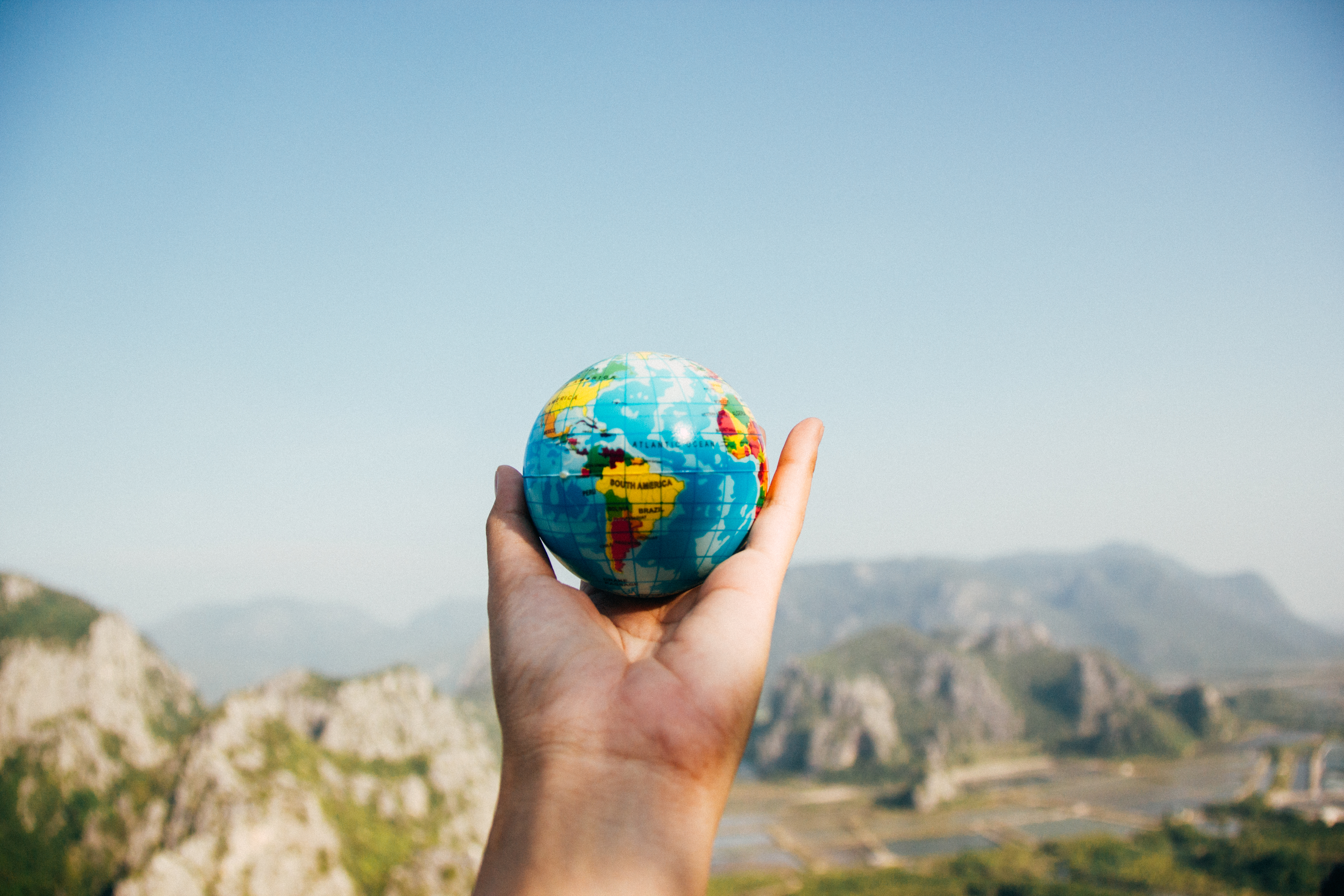 A hand holding a globe against a scenic mountain landscape