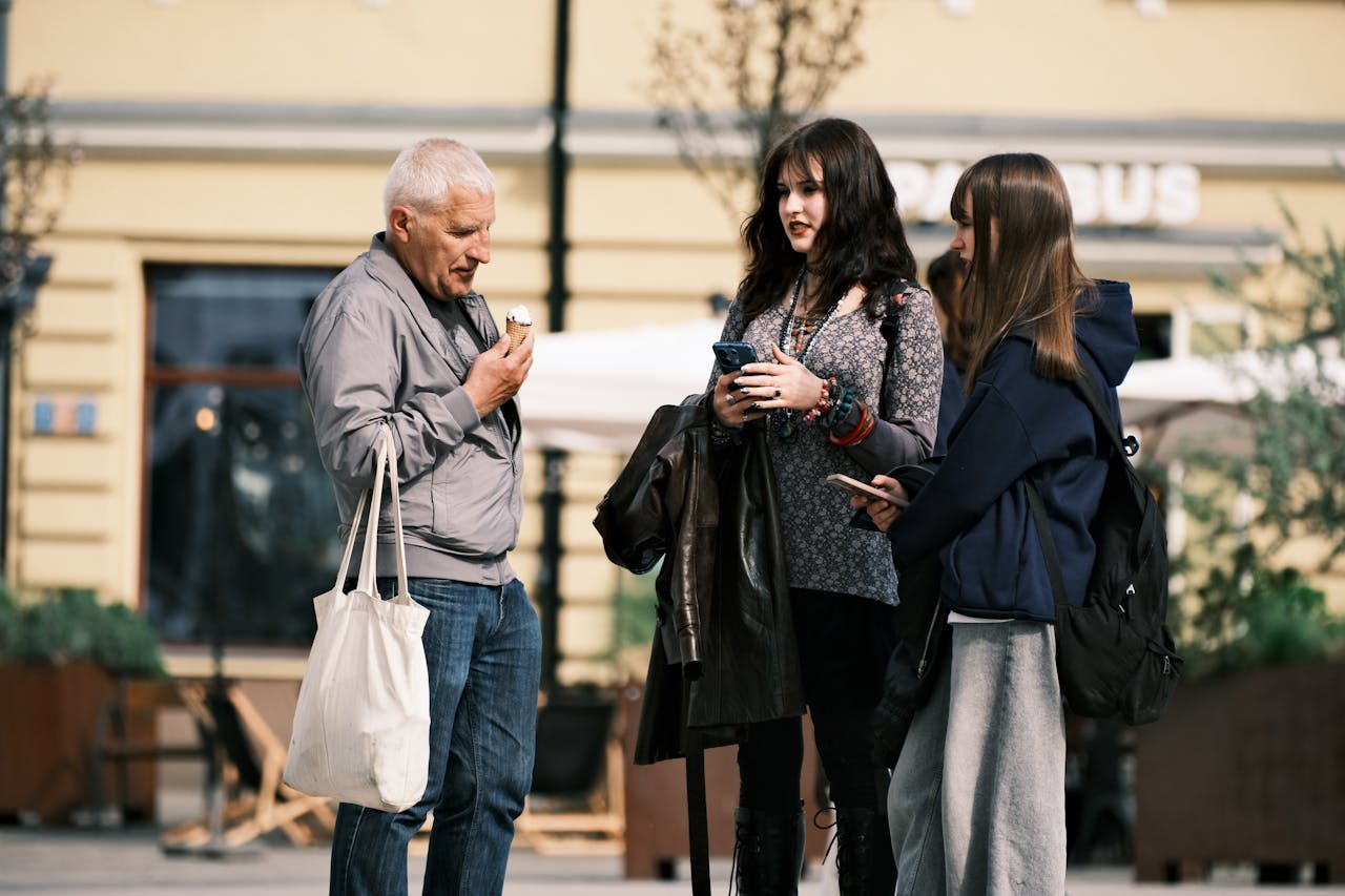 Three people standing outdoors; one eating an ice cream, two using phones.