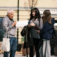 Three people standing outdoors; one eating an ice cream, two using phones.