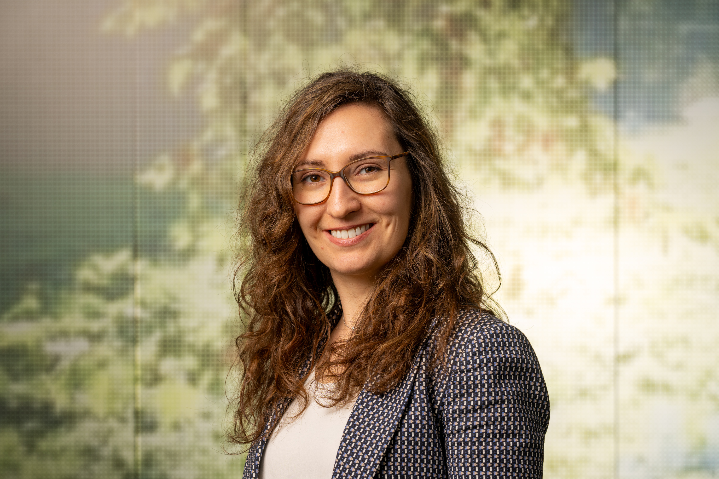 woman smiles at the camera with a background image of foliage behind her