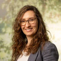 woman smiles at the camera with a background image of foliage behind her