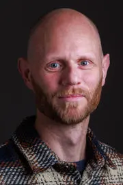 Professor Aaron Reeves headshot, he is smiling against a black backdrop.