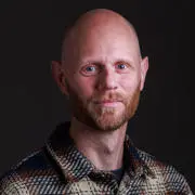 Professor Aaron Reeves headshot, he is smiling against a black backdrop.