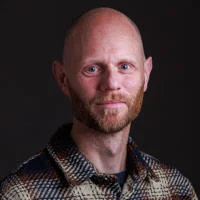 Professor Aaron Reeves headshot, he is smiling against a black backdrop.