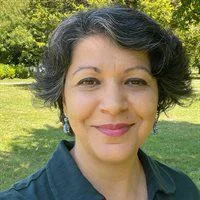 A close-up photo of Sana Murrani with trees and grass in the background.