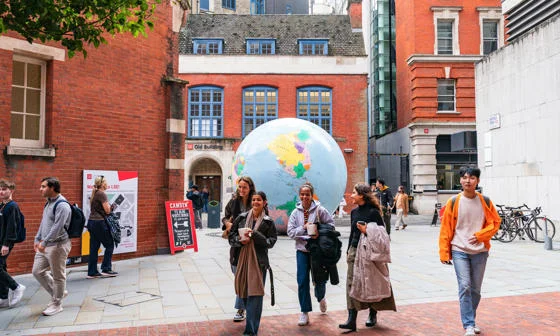 Students walking on campus in front of "The World Turned Upside Down" sculpture.