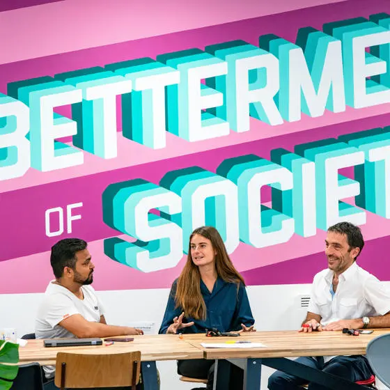 Students at a desk in front a wall emblazoned with the LSE motto, For the betterment of society