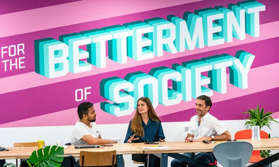 Students at a desk in front a wall emblazoned with the LSE motto, For the betterment of society