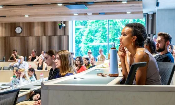 Students seated in a modern lecture theatre, listening to a speaker at the front of the room.