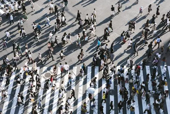 Aerial view of a crowded pedestrian crossing in a city, with people walking in multiple directions.