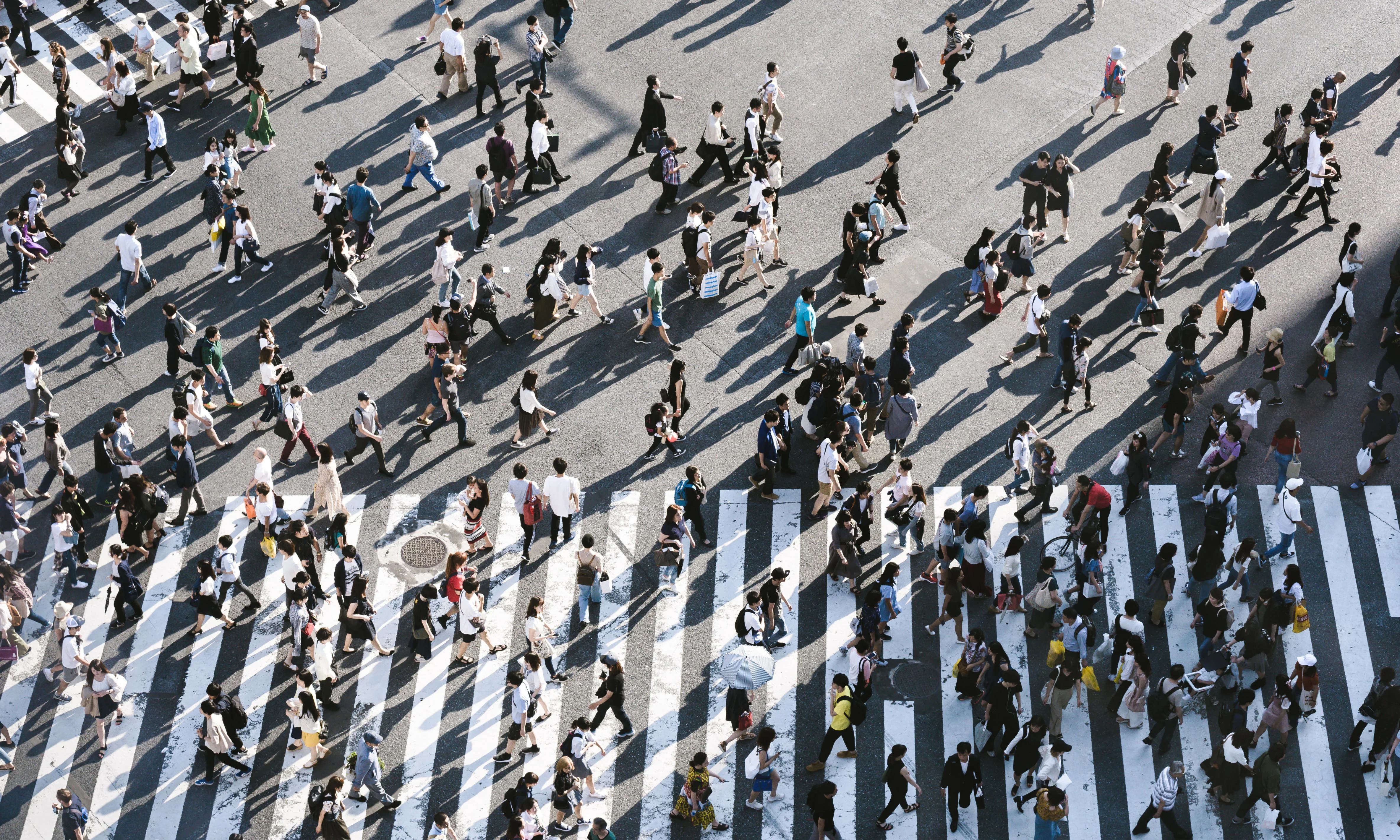 Aerial view of a crowded pedestrian crossing in a city, with people walking in multiple directions.
