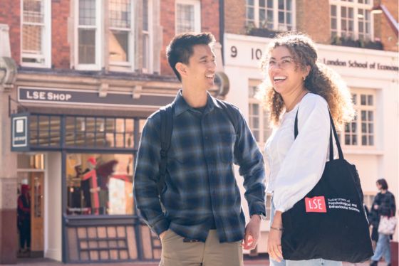 Two students walking and chatting outside on campus, with the LSE Shop visible in the background.