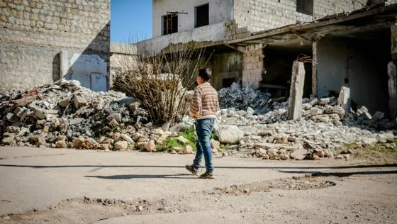 A child walks past the rubble of a heavily damaged building.