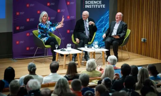Three panelists sit and laugh on stage