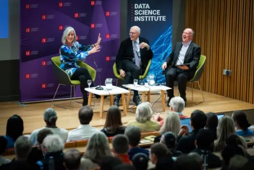 Three panelists sit and laugh on stage