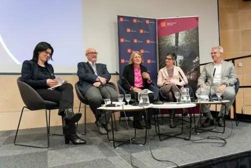 Five panellists sit in a discussion at an event