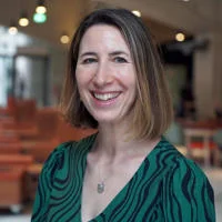 Rachel is wearing a green blouse and facing the camera at a slight angle. She is smiling.
