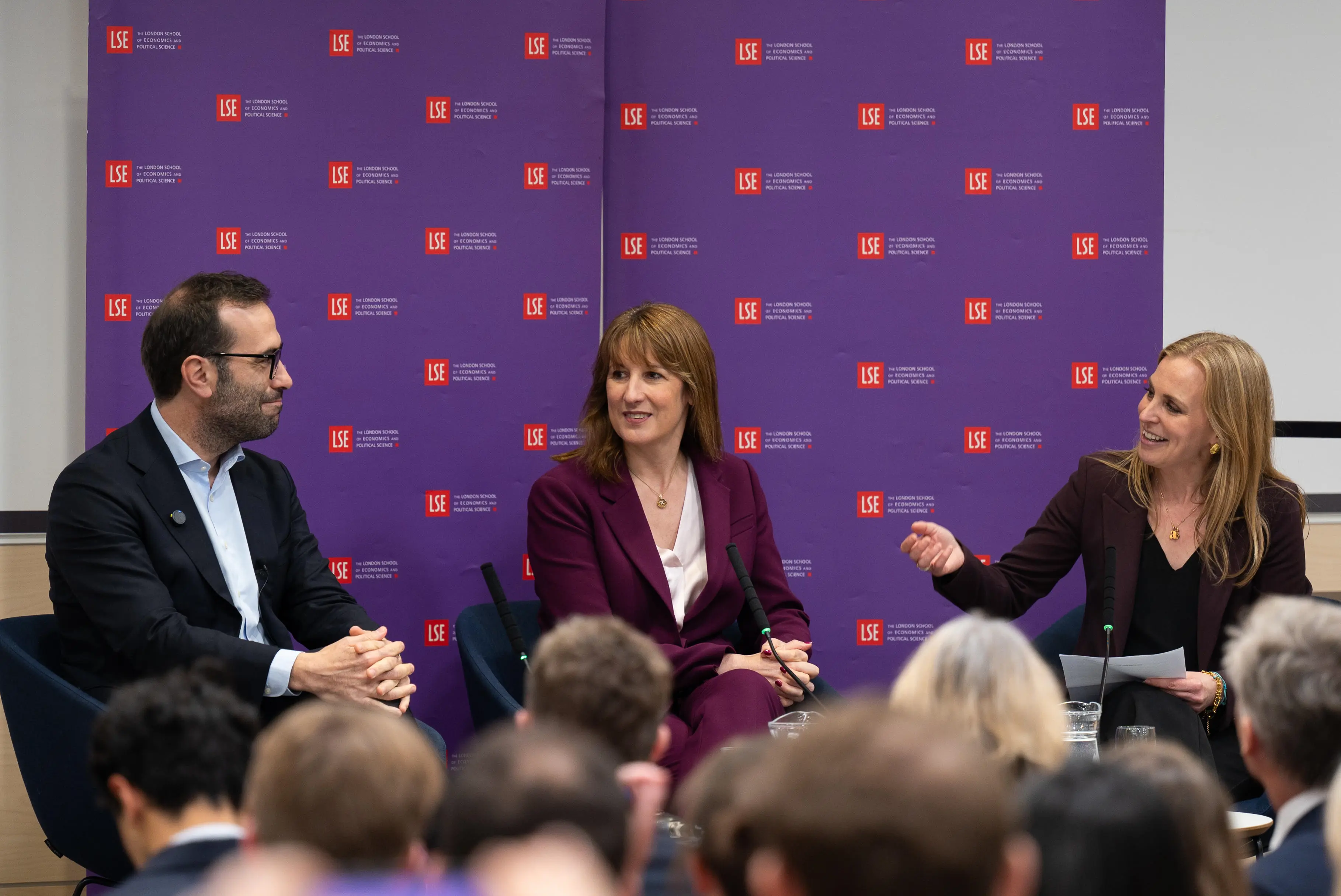 Anna Valero talks to Carlos Cuerpo and Rachel Reeves MP in front of a purple screen of LSE logos.