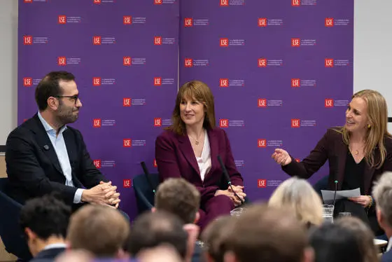 Anna Valero talks to Carlos Cuerpo and Rachel Reeves MP in front of a purple screen of LSE logos.