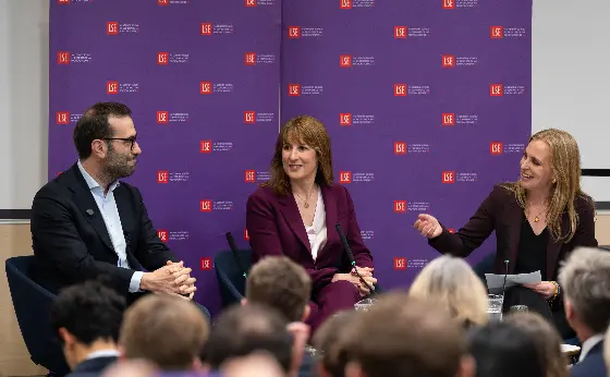 Anna Valero talks to Carlos Cuerpo and Rachel Reeves MP in front of a purple screen of LSE logos.