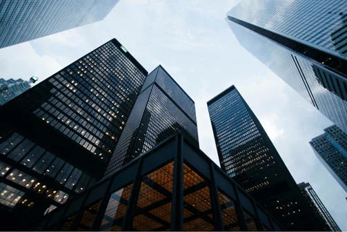 Buildings in a city, shot from below and facing upwards with a grey sky above.