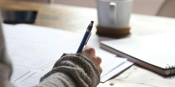 A hand holding a pen writing on a piece of paper