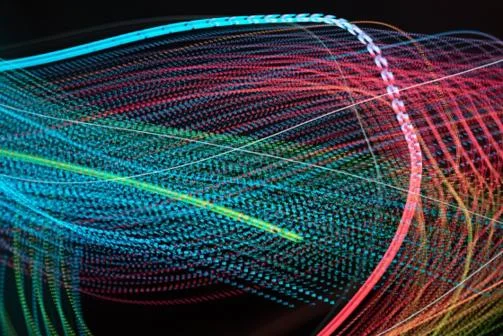 Abstract image featuring intertwined strands of vibrant colours, including blue, red, and yellow, against a dark background.