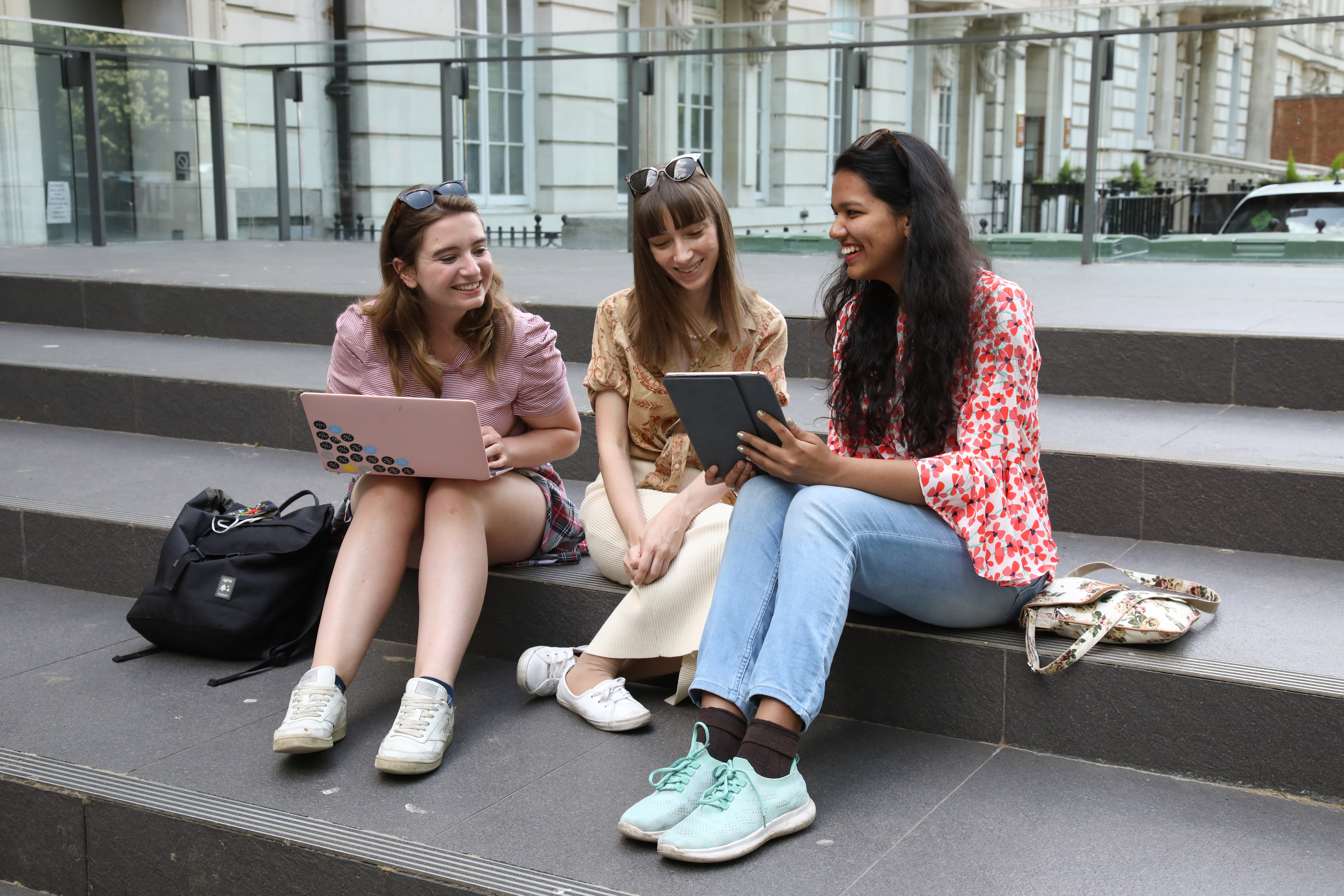 A group of students sitting on the steps of an LSE building, holding laptops and smiling