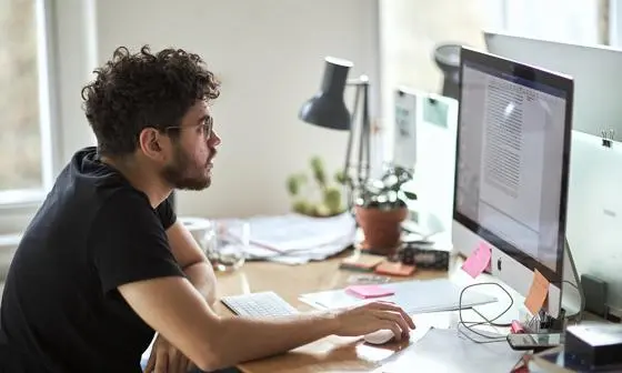Man sits at a messy desk working on a computer