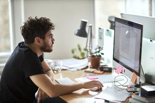 Man sits at a messy desk working on a computer