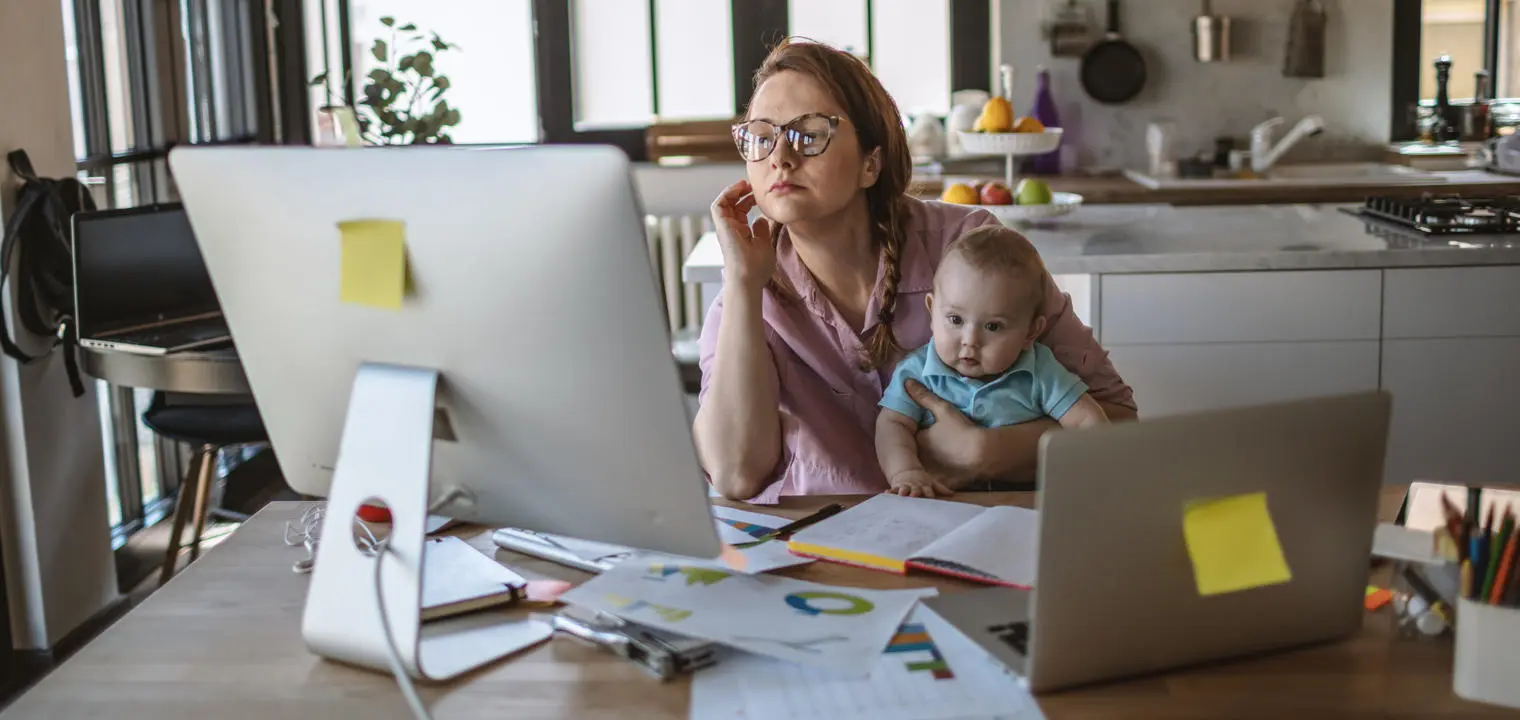 A woman works at a computer while holding a baby.