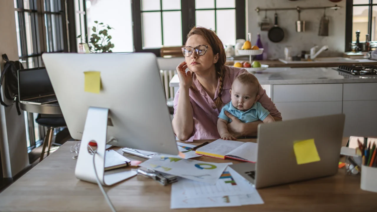 A woman works at a computer while holding a baby.