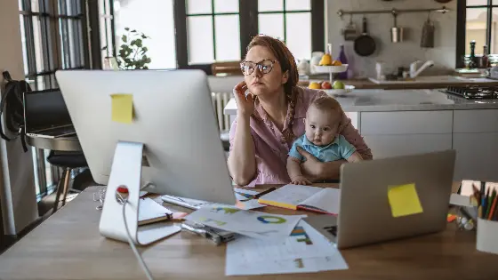 A woman works at a computer while holding a baby
